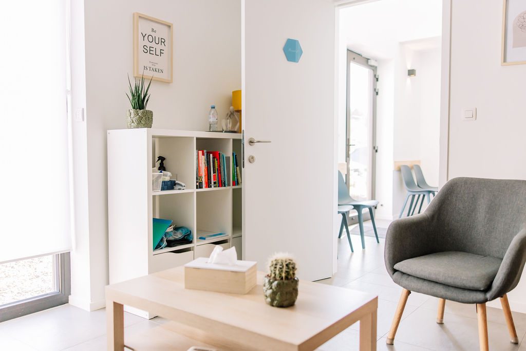 Een lichte spreekruimte met fauteuil en boekenkast in de praktijk